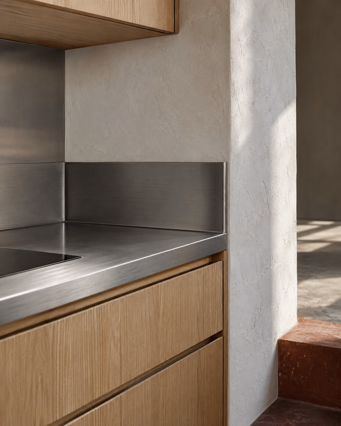 Close view of oak cabinetry meeting mineral plaster and a brushed steel worktop, with the joints aligned
